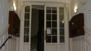 Una imponente escalera conduce a una puerta con paneles de vidrio, flanqueada por armarios de madera y apliques de pared.