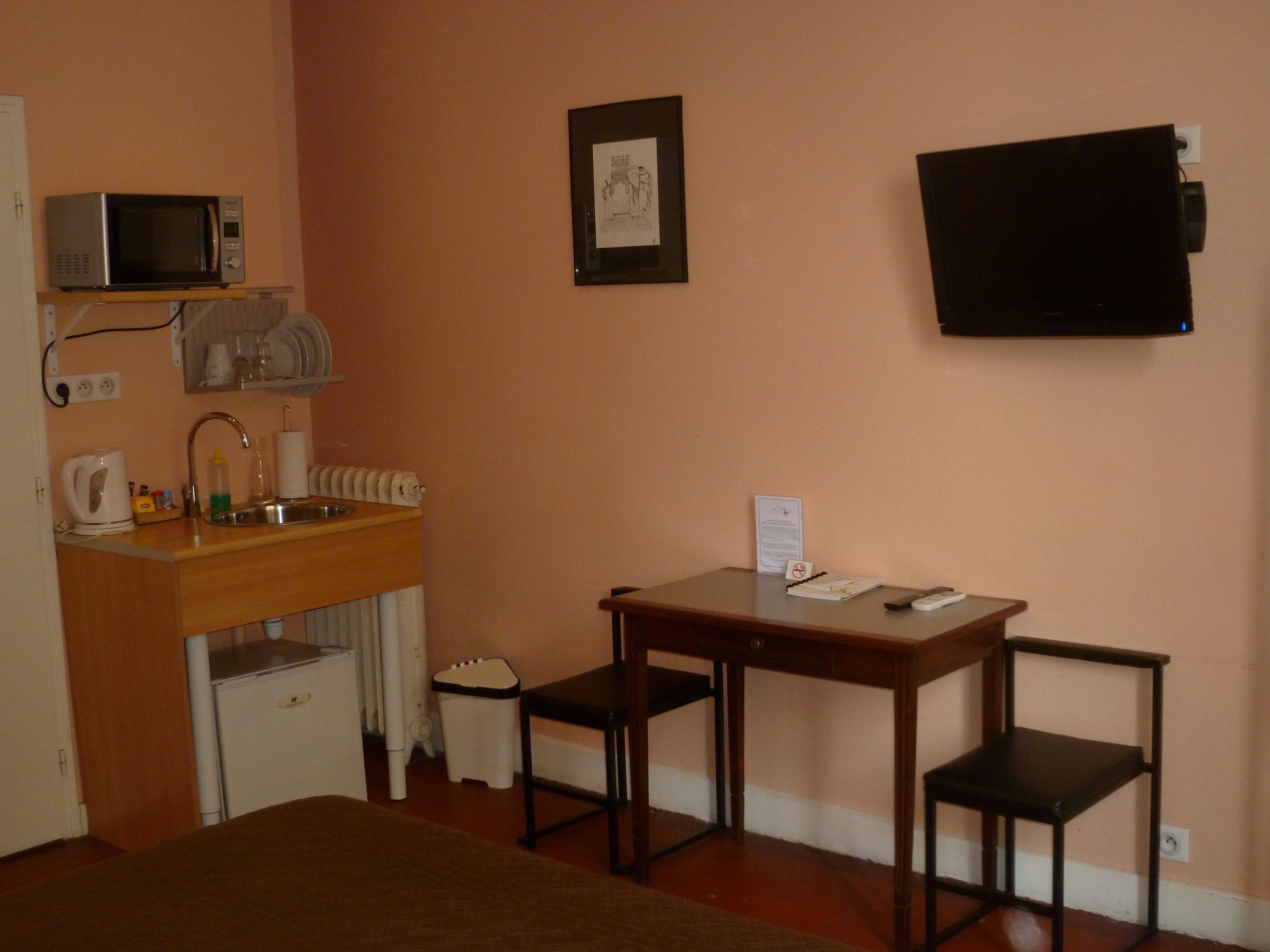 Habitación de hotel pequeña con kitchenette, cama, una mesita con sillas, televisor y un cuadro en la pared.