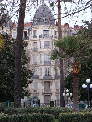A multi-story building with balconies, surrounded by trees and a fence.