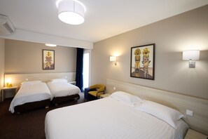 A hotel room with two beds, a chair, a nightstand, and wall-mounted lamps.