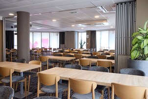 Une chambre d’hôtel avec plusieurs tables et chaises, une grande colonne et une plante en pot.