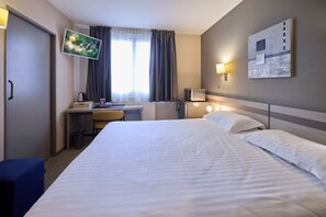 A hotel room with a bed, desk, chair, TV, and artwork on the wall.