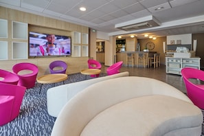 A modern hotel lobby with a TV, seating area, bar, and reception desk. - Park Hôtel (Cholet)