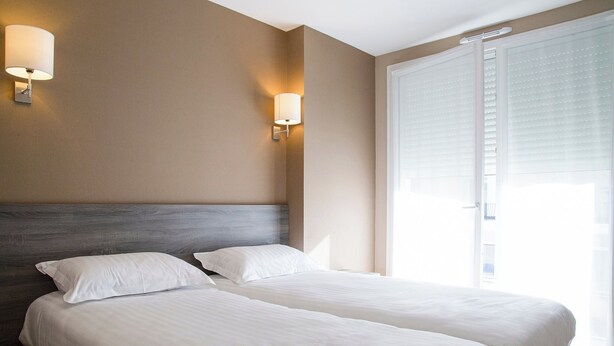 Habitación de hotel con dos camas, cabecera, lámparas fijadas a la pared y un ventanal con persianas.