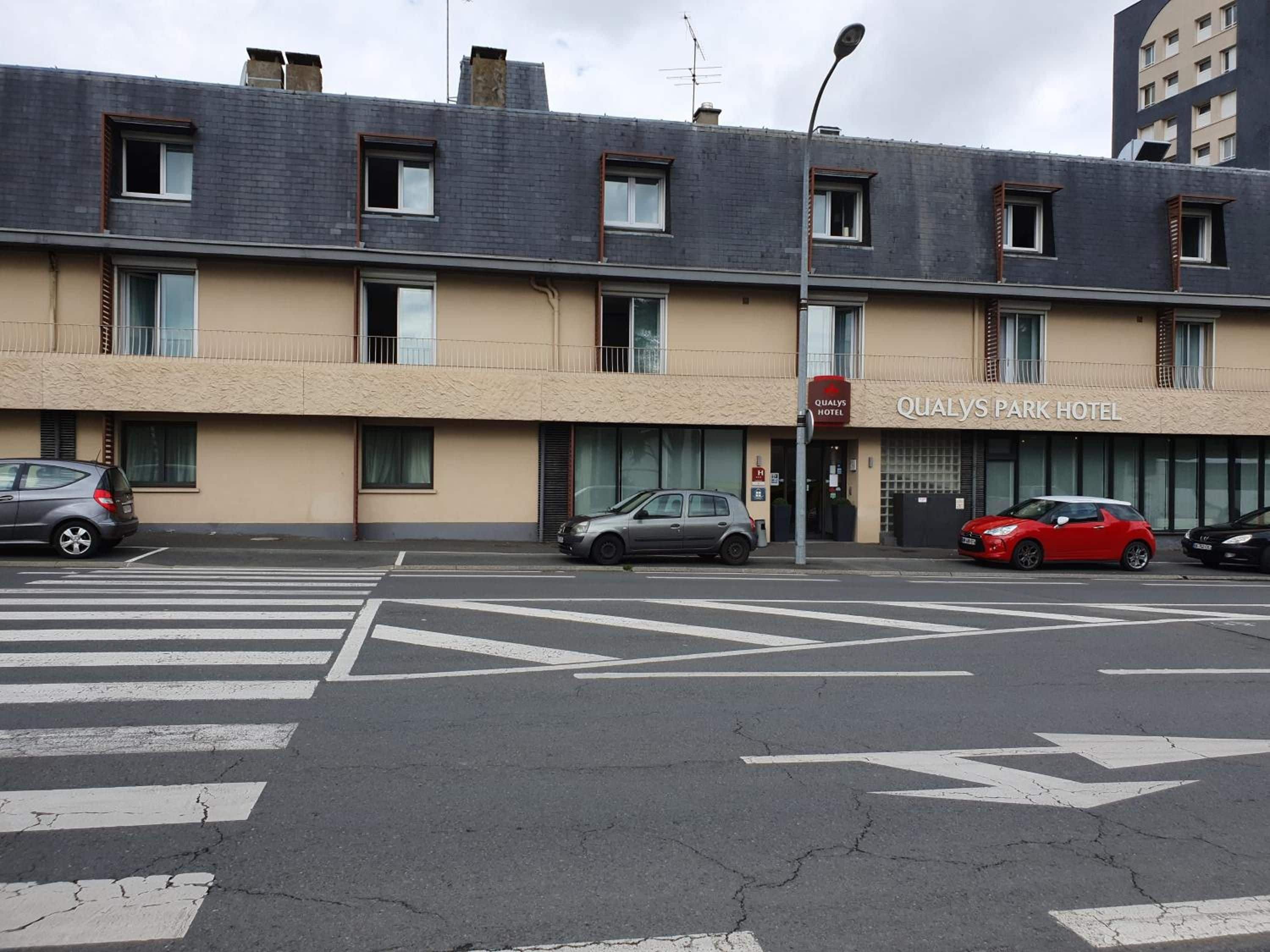 A building with a sign for Qualys Park Hotel, featuring a crosswalk and parked cars.