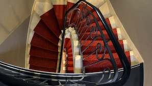 Una escalera en espiral con peldaños cubiertos de alfombra roja y barandilla de metal negro.