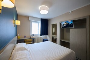A hotel room with a bed, a desk, a chair, a radiator, a television, and a wardrobe.