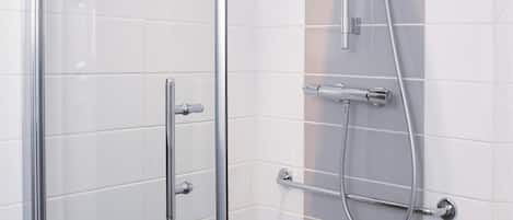 Zona de ducha con mampara de vidrio, cabezal de ducha de mano y grifo empotrado en la pared.
