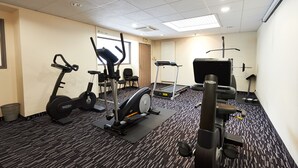 Un gimnasio con máquinas de cardio, cinta de correr y banco para pesas.