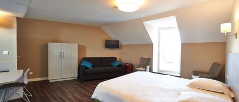 A hotel room with a bed, a desk, a chair, a sofa, and a TV.