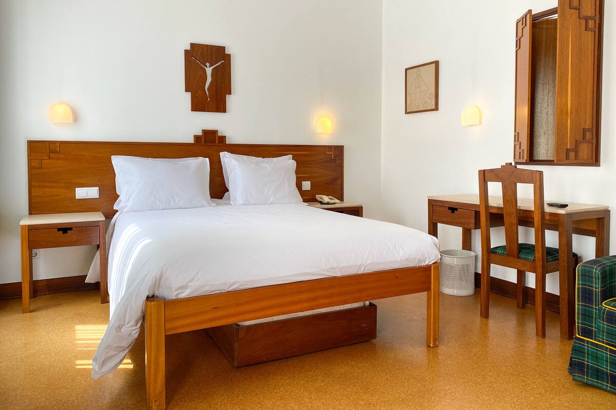 Une chambre d’hôtel avec un lit en bois, des tables de chevet, un bureau et une chaise.
