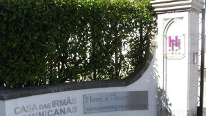 A sign for Casa das Irmãs Min Canas Hotel e Restaurante with a stone wall and a hedge in the background. - Flag Hotel Fátima Irmãs Dominicanas (Ourem)