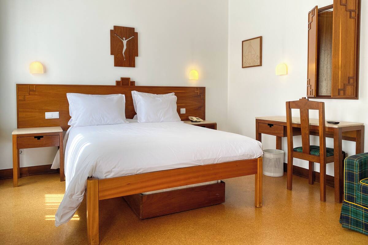 Une chambre d’hôtel avec un lit en bois, des tables de chevet, un bureau et une chaise.