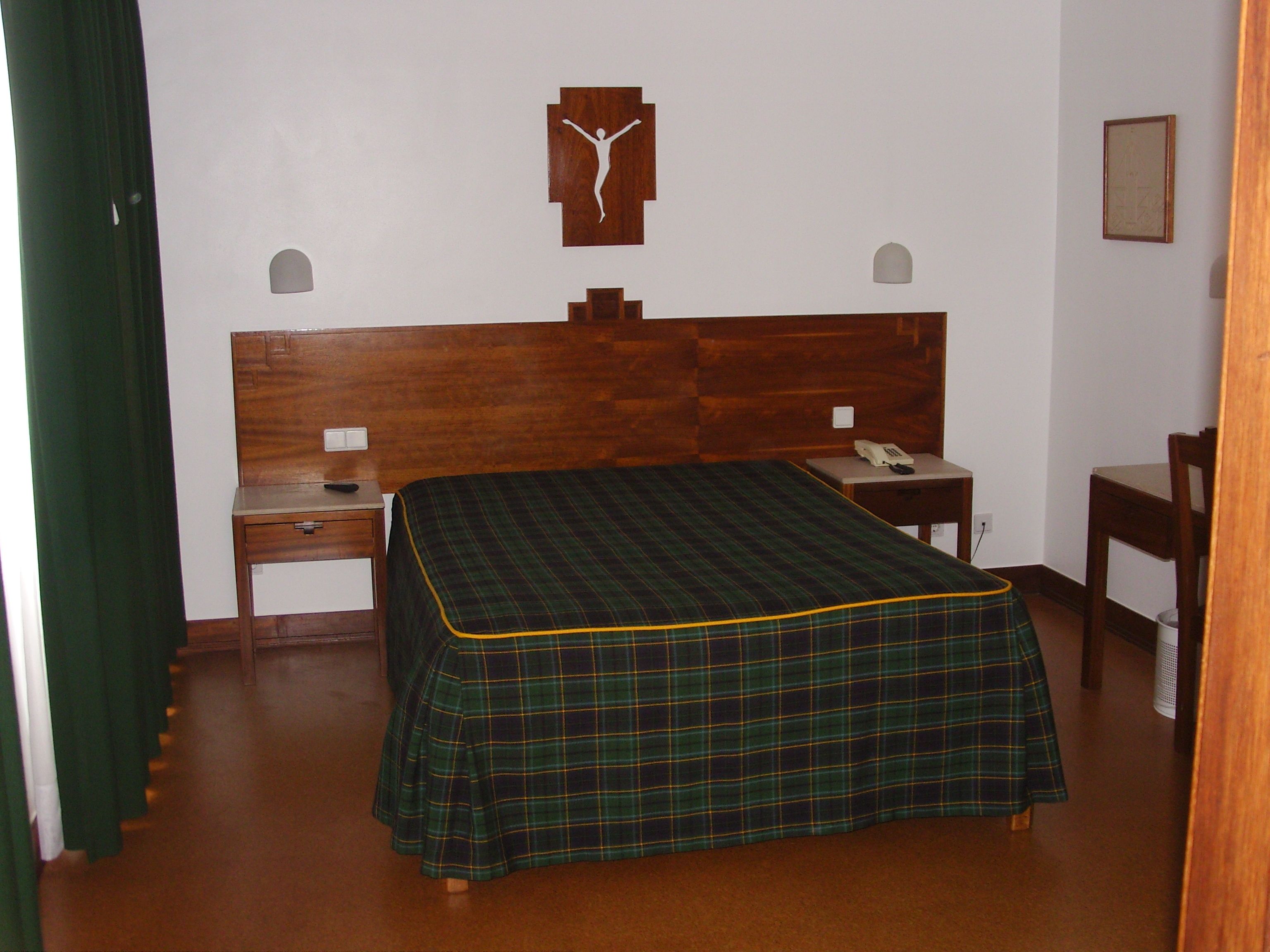 A room with a wooden bed, a nightstand, a chair, and a wall-mounted artwork.