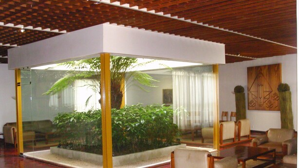 A modern living room with a glass partition, a large plant, and a seating area with chairs and a sofa. - Flag Hotel Fátima Irmãs Dominicanas (Ourem)