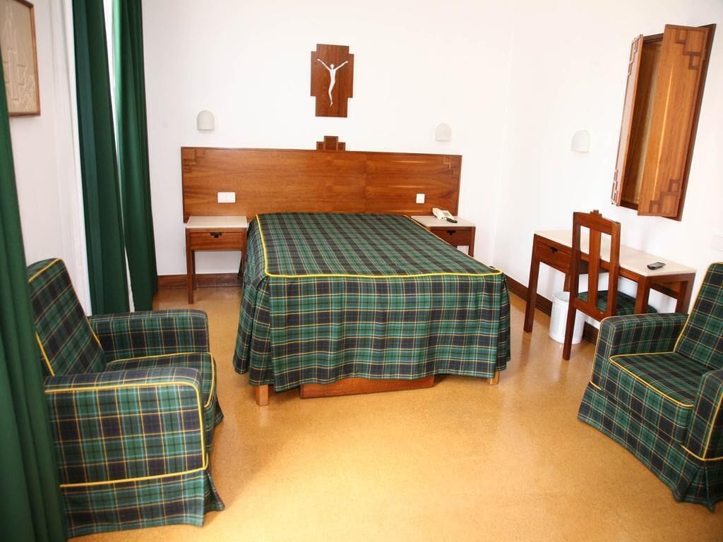 Een kamer met een bed, twee stoelen, een bureau en een spiegel.