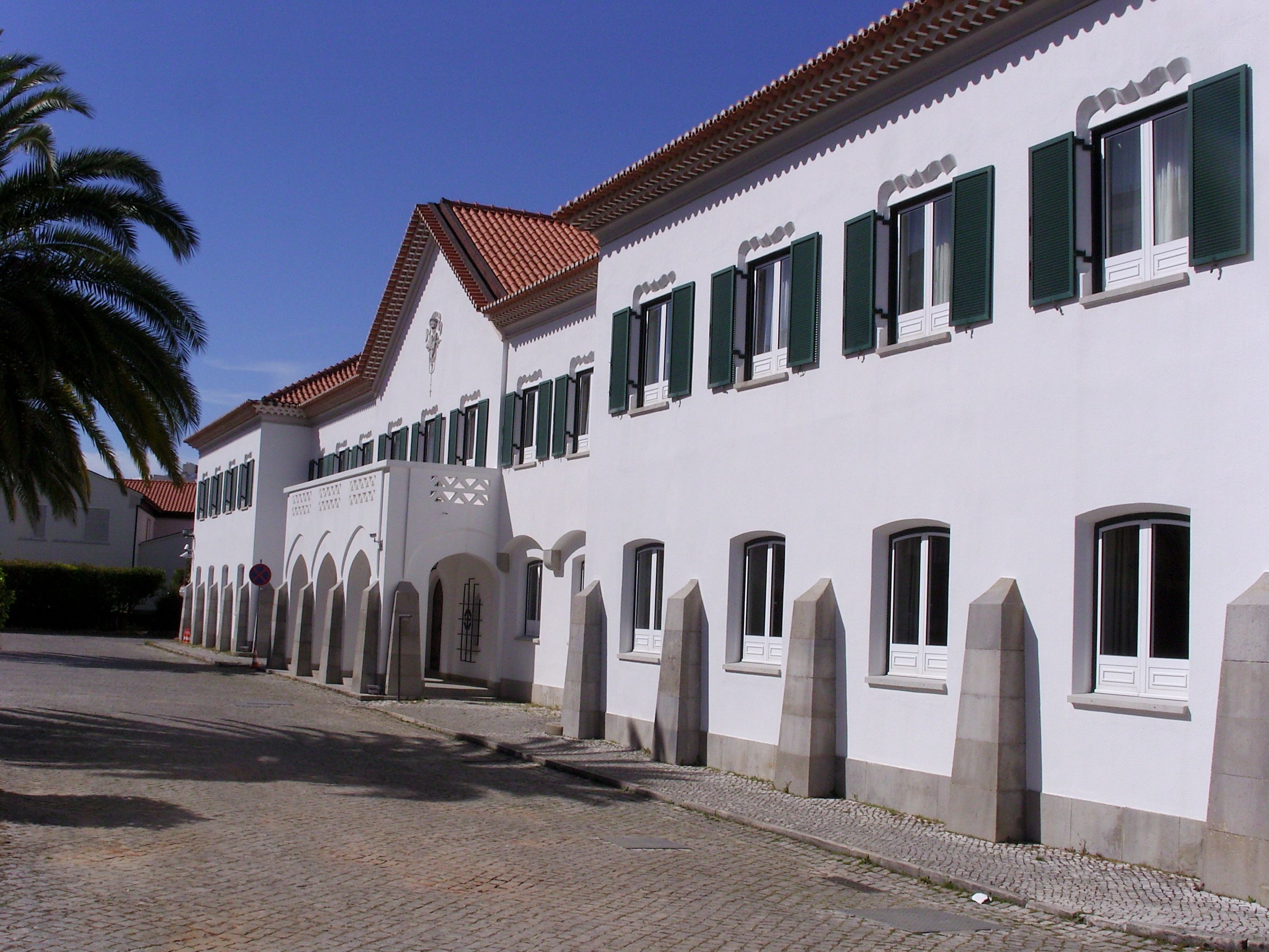 A white building with green shutters and a tiled roof.