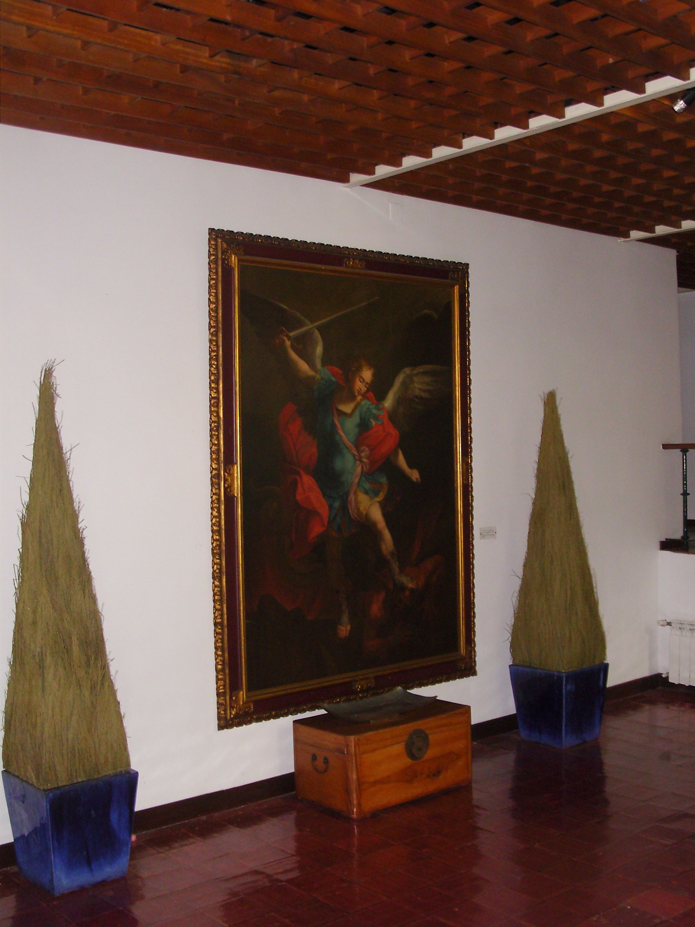 A room with a large framed painting on the wall, a wooden chest, and two conical vases.