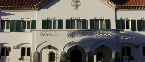 A building with a white facade, green shutters, and a tiled roof.