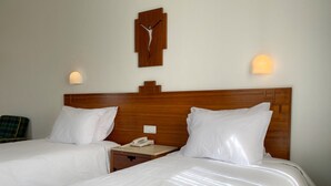 A hotel room with two beds, a wooden headboard, a bedside table with a phone, and a wall-mounted light fixture. - Flag Hotel Fátima Irmãs Dominicanas (Ourem)