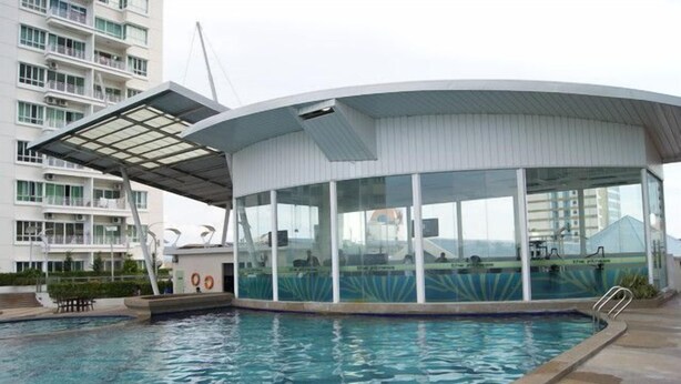A modern pool area with a glass-enclosed structure, a clear pool, and a view of a high-rise building in the background.