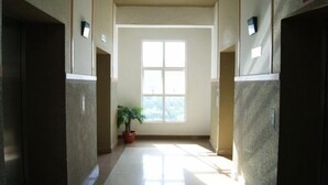 A corridor with a large window at the end, a potted plant, and a sign indicating a lift bomb shelter.