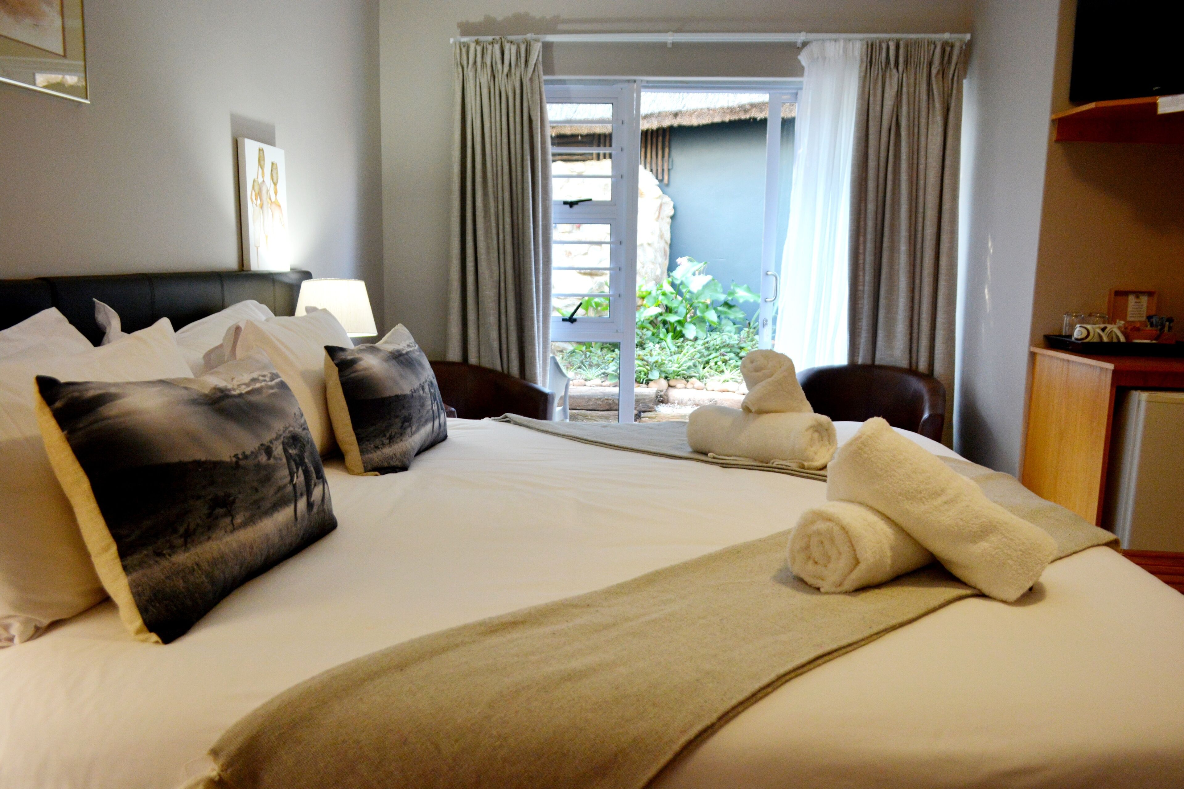 A hotel room with a bed, pillows, a blanket, a chair, and a view of the outside.
