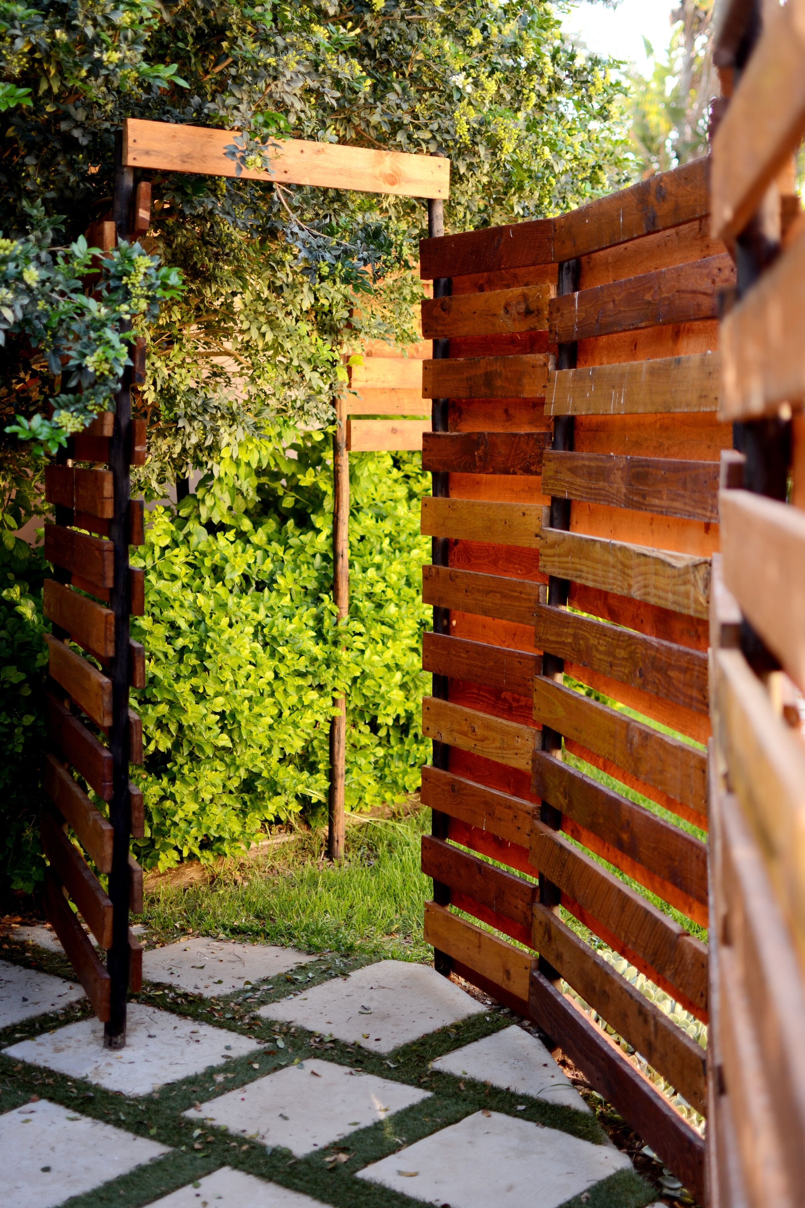 A wooden pergola structure with a lattice design, surrounded by lush green foliage.