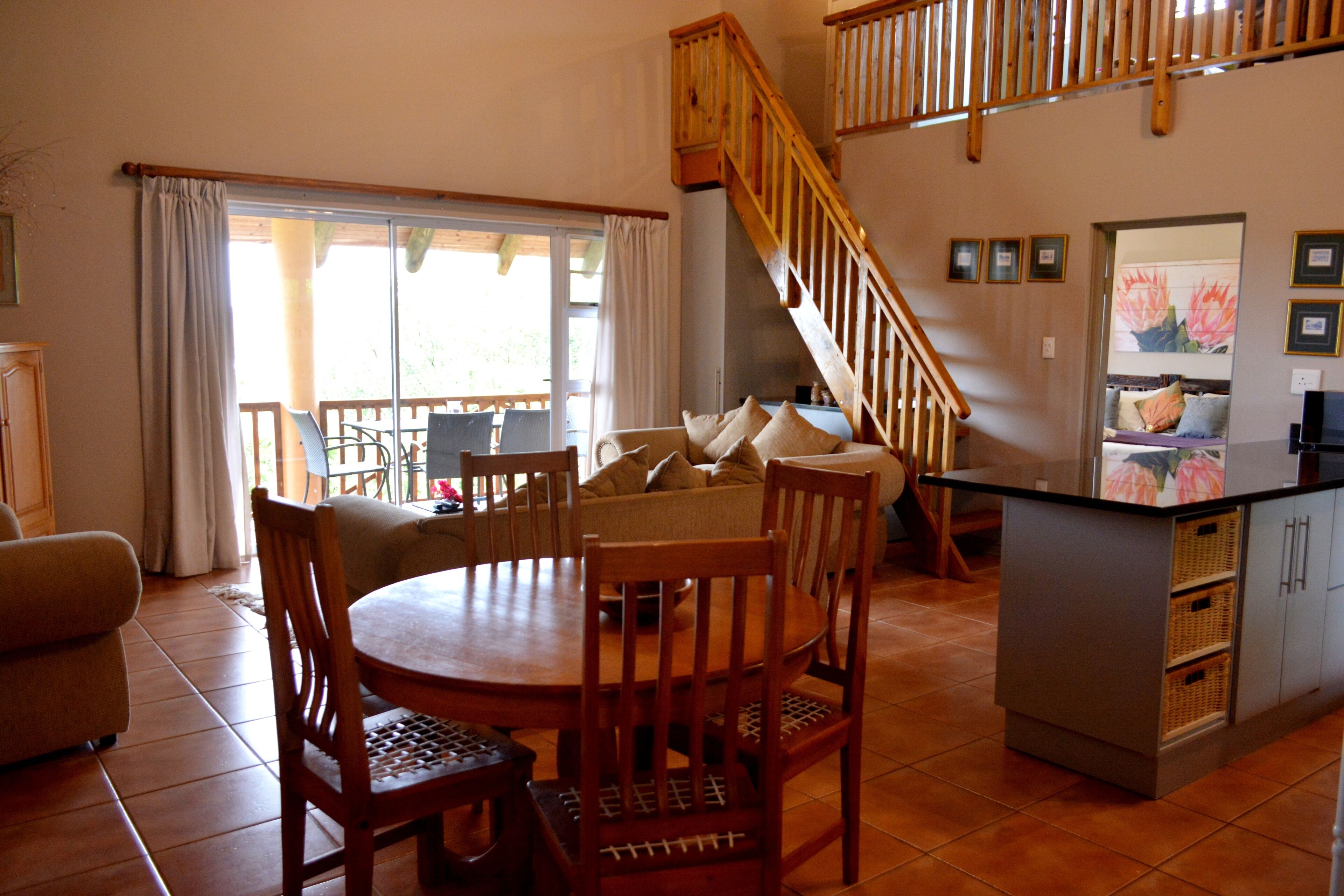 A spacious living area with a dining table, chairs, a sofa, a staircase, and a kitchen island.