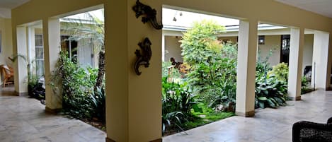 A spacious indoor area with a tiled floor, several columns, and a variety of plants.
