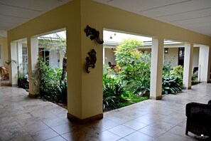 A spacious indoor area with a tiled floor, several columns, and a variety of plants. - Kududu Guest House (Addo)