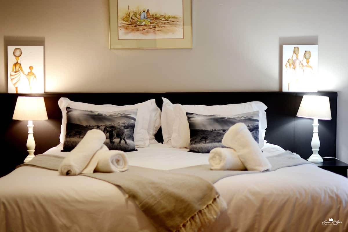 A neatly made bed with white linens and two pillows, each with a black and white landscape print. There are two bedside lamps on either side of the bed.