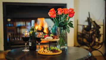 Una mesa con una botella de vino, dos copas, un plato de aperitivos y un florero con rosas.