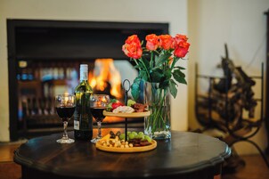 Una mesa con una botella de vino, dos copas, un plato de aperitivos y un florero con rosas.