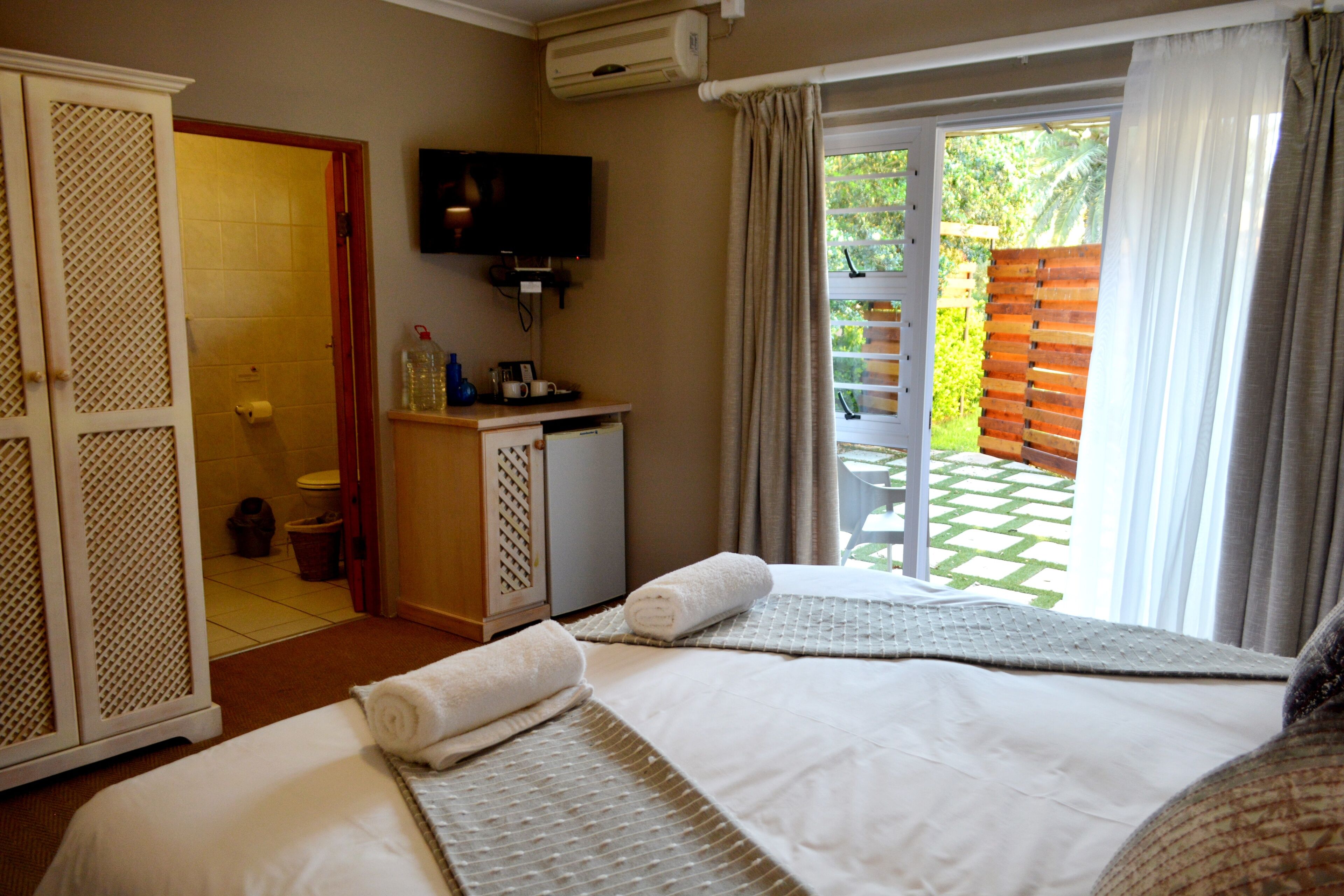 A hotel room with a bed, a television, a desk, and a view of the outside.