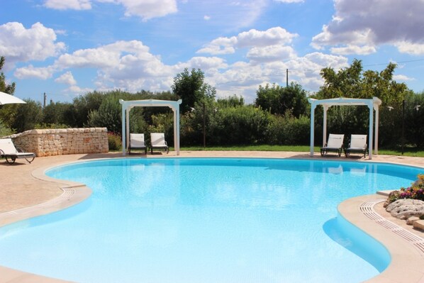 A swimming pool with two gazebos, lounge chairs, and a stone wall.