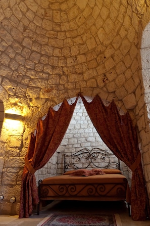 A stone-walled room with a bed, a stone ceiling, and a wall-mounted light fixture.