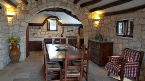 Una cocina rústica de piedra con una gran mesa de madera, sillas y una chimenea de piedra.