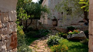 Un camino de piedra que lleva a un edificio de piedra con chimenea, rodeado de follaje y flores.