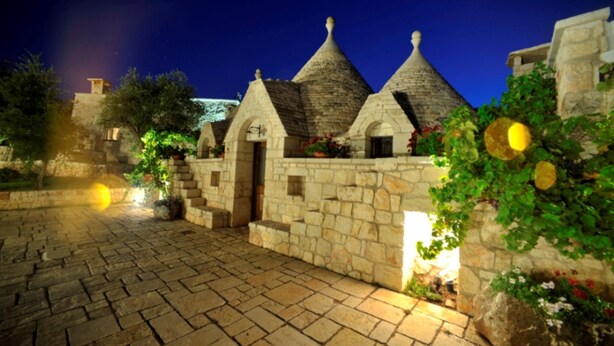 Un edificio de piedra con techos cónicos, un patio empedrado y vegetación circundante.