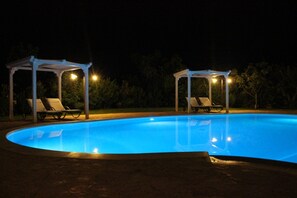 A swimming pool with two covered areas and lounge chairs.