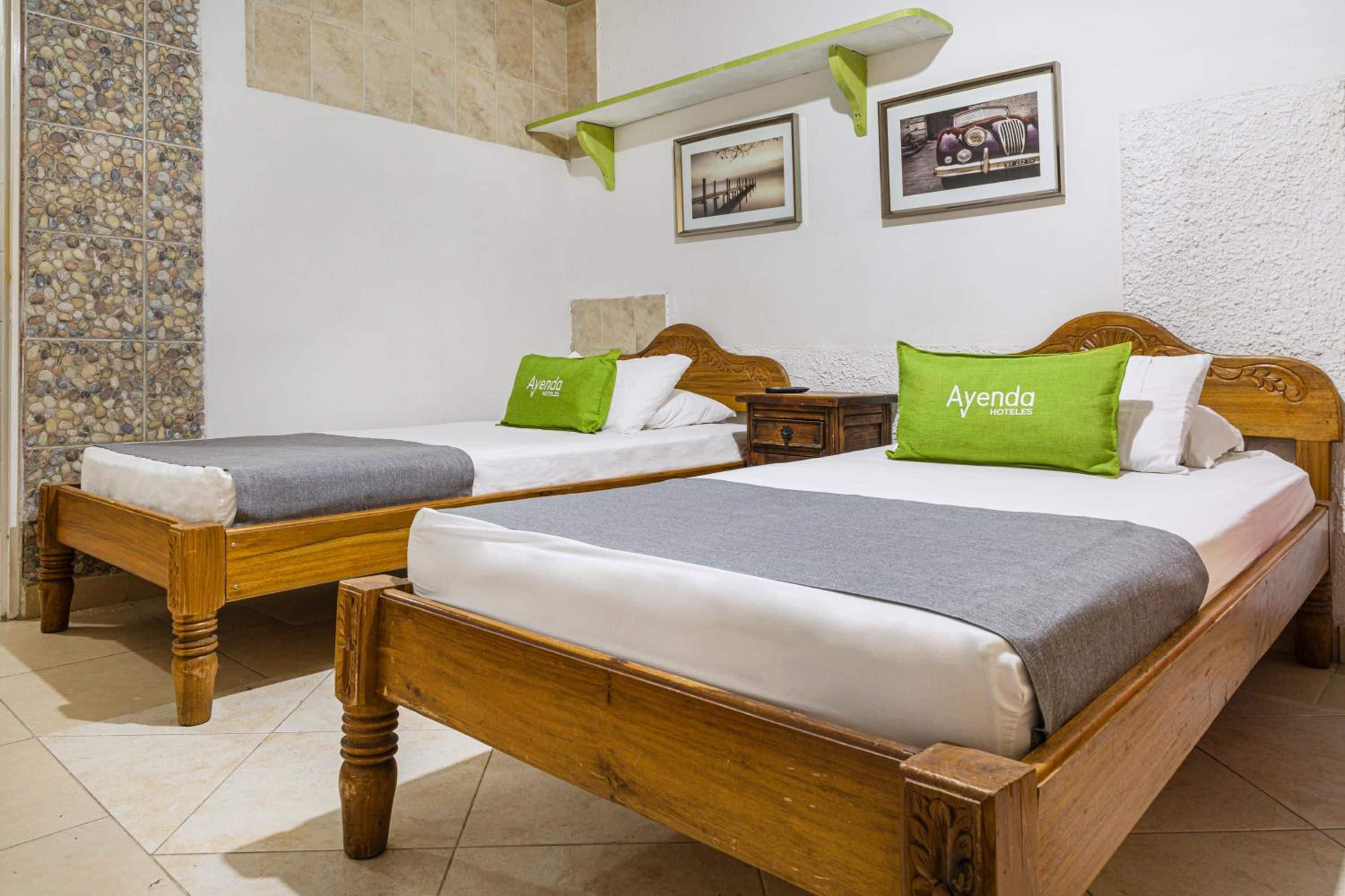 A hotel room with two wooden beds, each with a pillow and a blanket. There are two framed pictures on the wall.