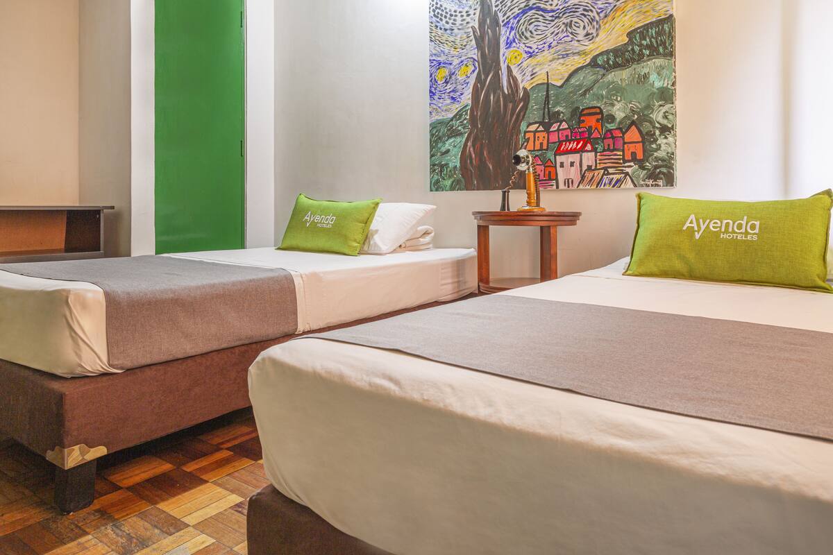 Une chambre d’hôtel avec deux lits, chacun étant équipé d’un oreiller portant la mention « Ayenda Hotels ».