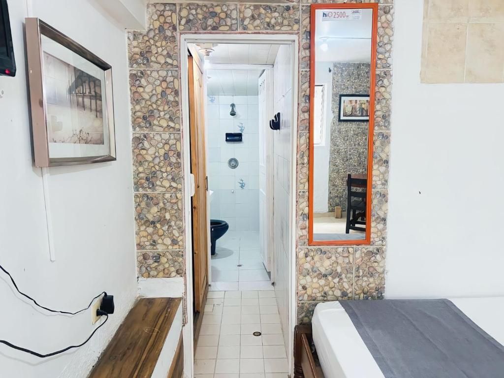 A narrow hallway leading to a bathroom with a shower and toilet. A bed is visible in the foreground with a wooden floor.