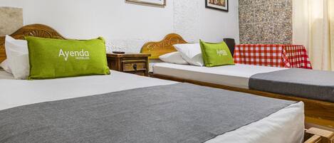 Habitación de hotel con dos camas, cada una con un almohadón verde con la etiqueta 'Ayenda Hotels'.