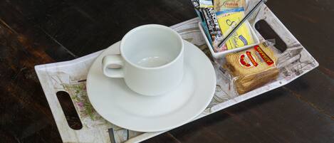 A tray with a white cup, a sandwich, and some packaged food items on a dark wooden table.