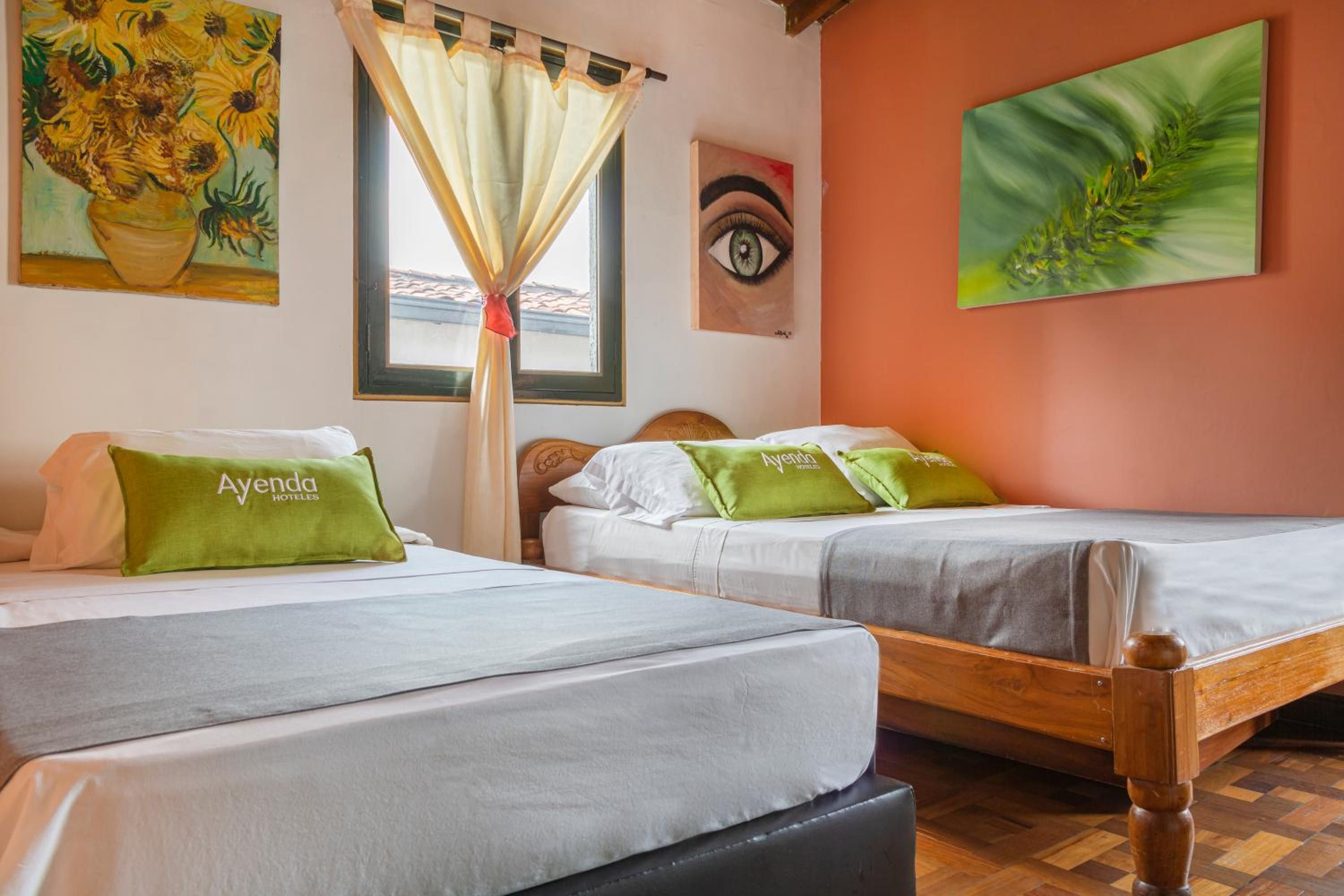 Una habitación de hotel con dos camas, una ventana con cortinas y obras de arte en las paredes.