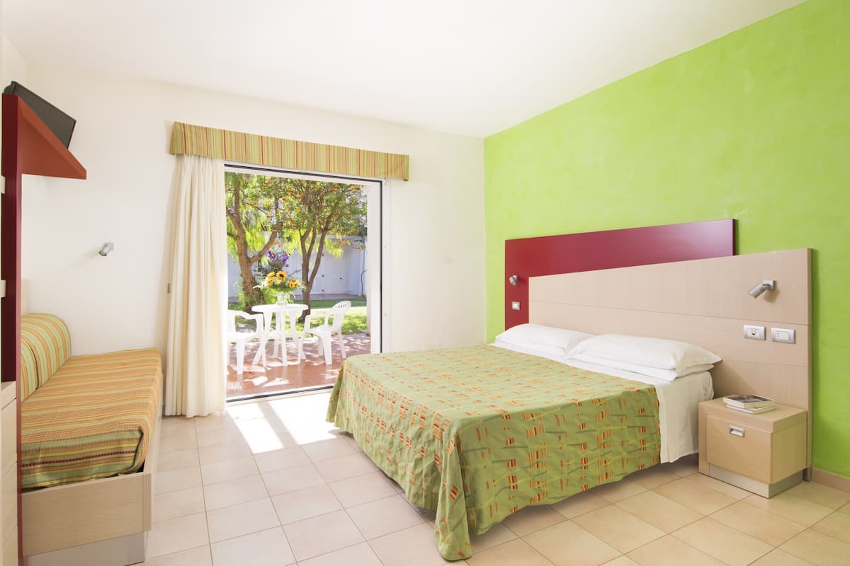 Quarto de hotel com cama, mesa de cabeceira, cadeira e vista para o exterior.