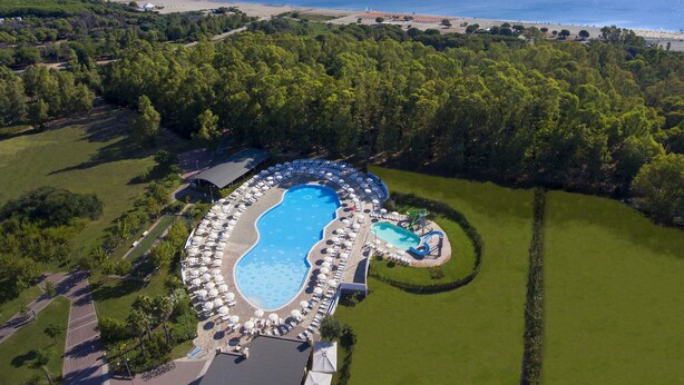 Vista aérea de un complejo turístico con una gran piscina, zonas de descanso y una playa.
