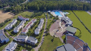 Vista aérea de un complejo turístico con piscina, varias edificaciones y una playa.